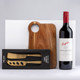 A drink bottle of red wine alongside a wooden cheese board and a gold two-piece cheese knife set, featuring a branded box. A drink bottle of red wine alongside a wooden cheese board and a gold two-piece cheese knife set, featuring a branded box.
