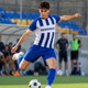 A player in a blue and white striped jersey kicks a soccer ball on a field, with teammates in the background.