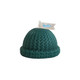 A green candle shaped like a knitted beanie, featuring a small flag with a logo.