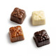 A selection of four chocolate squares in dark, milk, and white chocolate, each shaped like a gift with ribbon detailing.