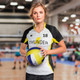 A woman in a black, white, and yellow volleyball jersey holds a volleyball. The jersey features a logo and number 18. A woman in a black, white, and yellow volleyball jersey holds a volleyball. The jersey features a logo and number 18.