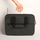 A black laptop bag with handles, featuring a zippered compartment, being held above a laptop.