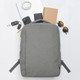 A grey backpack surrounded by a notebook, sunglasses, keys, phones, and a charger on a white background.