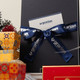 A customised gift set in a black box, tied with a blue ribbon featuring a logo, surrounded by festive decorations.