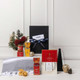 A customised gift set featuring festive treats, a grey throw, decorative items, and a black box with a ribbon.