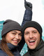 A grey beanie is worn by a man and a woman, both smiling and wearing winter jackets against a snowy backdrop.