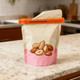 A large food bag seal clip in orange, securing a beige bag featuring illustrations of assorted nuts on a kitchen countertop.