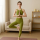 A green zip-front racerback yoga crop bra tank paired with matching leggings, showcased by a model in a living room setting.