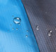 A water-resistant picnic blanket featuring a blue section and a grey section, with droplets of water on the surface.