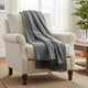 A grey throw blanket draped over an armchair in a bright room, with a plant and table nearby.