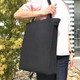 A foldable black calico tote bag with handles, held by a person against a backdrop of greenery.