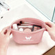A pink silicone cosmetic bag with various beauty products and tools inside, featuring a logo on the front.
