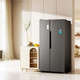 A black fridge stands beside a light wooden cabinet in a bright, modern space. The fridge features a logo on its door.