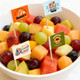 A bowl of mixed fruit featuring watermelon, grapes, and melon, decorated with branding flag sticks.