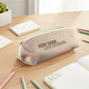 A beige pencil case with a zip closure sits on a wooden desk among stationery and notepads. It features a logo.