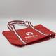 A red canvas tote bag with white striped handles and a logo on the front.
