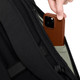 A black backpack with a grey pocket, featuring a person placing a brown phone into the pocket.