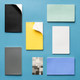 A collection of notebooks in various colours including black, yellow, white, grey, mint green, and blue, lying on a blue surface.