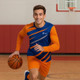 A man in a blue and orange sports long sleeves shirt dribbles a basketball on a gym court. The shirt has a logo.