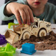 A wooden model of a wheel loader in natural wood colour, surrounded by coloured plastic moulds and sand.