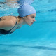 A premium silicone swimming cap in light blue, featuring a textured design, submerged underwater with a swimmer.