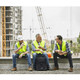 Three men in reflective vests sit together on a construction site, discussing beside a black High Sierra Access 4.0 Backpack.