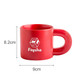 A red ceramic coffee mug with a unique handle design and a logo printed on the side. Dimensions are 8.2 cm high and 9 cm wide.