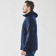 A man is wearing a navy blue wind jacket featuring a hood and a logo, shown from the side.