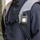 A compact black multi-tool attached to a backpack strap, featuring a bright LED light.