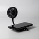 A black rechargeable fan with a flexible neck, positioned next to a mobile phone on a flat surface. It features a branding logo.