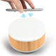 A wireless charger and speaker with a white top and bamboo base, featuring a hand holding a smartphone above it.