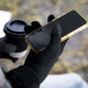 Black Himalayan Tech Gloves holding a smartphone, with a coffee cup partially visible in the background.