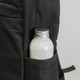 A black backpack pocket holds a silver-capped drink bottle, featuring a textured fabric design.