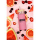A drink bottle with a pink exterior, wooden lid, and metal straw, surrounded by fresh fruit slices and berries.