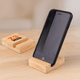 A bamboo phone holder with a black phone propped up, featuring a logo on the base, set on a wooden table.