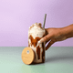 A drink bottle with a bamboo lid, featuring a creamy beverage topped with whipped cream, held in a hand.