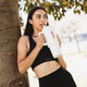 A drink bottle with a large white body and a straw, held by a person in a black sports outfit, leaning against a tree.