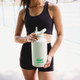 A drink bottle in light green with a flip-top spout, held by a person in activewear. It features a logo.