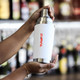 A drink bottle features a sleek white design with a stainless steel top and a logo. Ideal for beverages.
