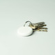 A white dual system item tracker sits alongside a set of metal keys on a light background. The tracker has a keyring attached.
