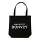 A black tote bag with handles, featuring a logo on the front, placed on a wooden table.