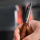 A wooden and metal ballpoint pen with a branding logo, being held in a hand.