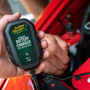 Hand holding the Battery Tender 022-0196 6V charger over the engine of a red classic vehicle
