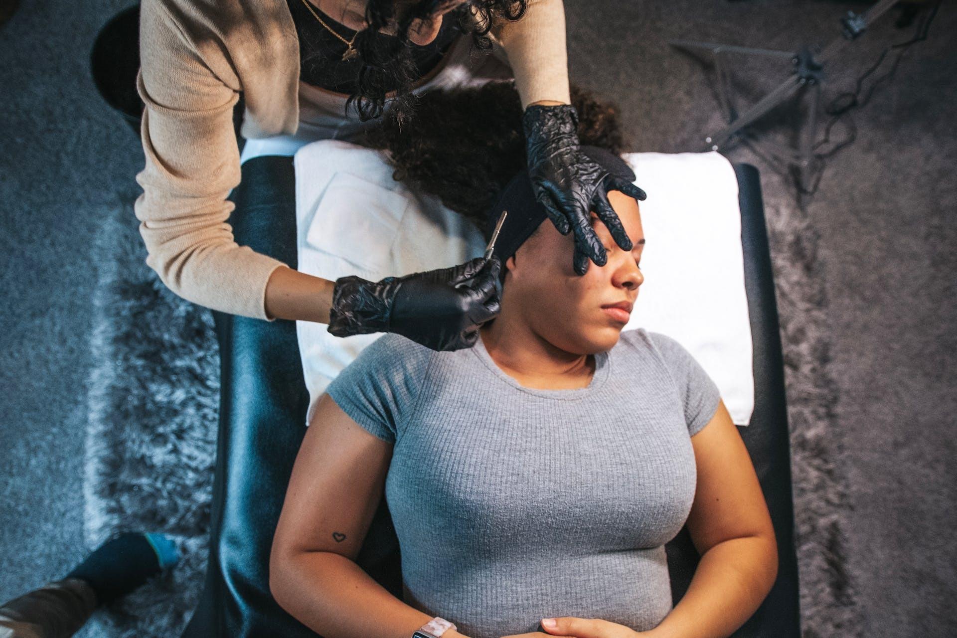 Person in black gloves waxing a client’s face