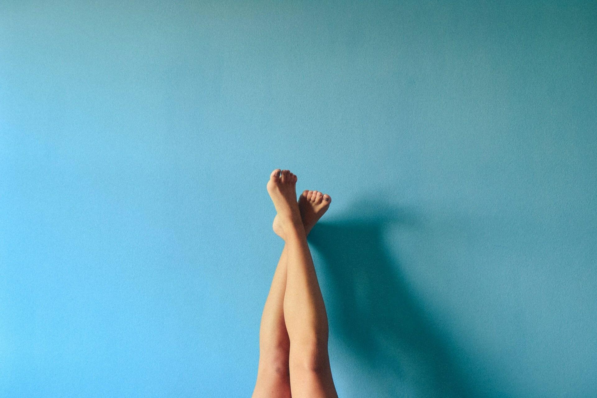 Smooth legs upright crossed at ankles against blue background