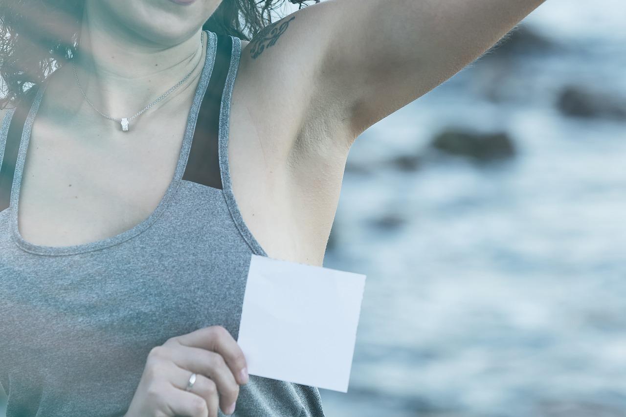 Woman with raised arm and smooth armpit holding square of paper