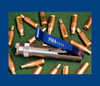 The PMA Mini Mite Priming Tool artfully displayed on a green background surrounded by scattered rifle cartridges. The priming tool is prominently featured with its polished silver body and distinctive blue handle, clearly marked with the 'PMA Tool' logo. This setup showcases the tool's practical use in the preparation of ammunition, emphasizing its essential role in hand-loading precision for shooting enthusiasts and professionals alike.