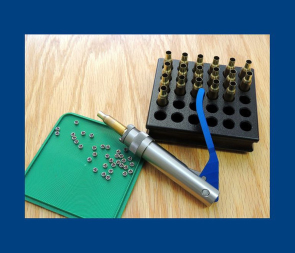 PMA Ball Bearing Drive Priming Tool set displayed on a wooden surface, including a metallic priming tool with a blue wrist strap, multiple primer casings on a green pad, and a black case with slots filled with brass casings.