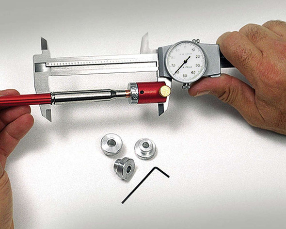 Hornady Lock-N-Load Comparator Body with a set of 7 inserts, model B234. The image shows a person using the comparator attached to a caliper to measure bullet dimensions. The comparator is equipped with different sized silver inserts and a red handle. This tool is essential for precision shooters and reloaders to ensure consistent bullet seating depths and enhance shooting accuracy.