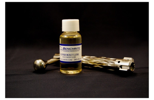 Dramatic display of a Benchrite Super Bolt Lube 1oz bottle, set against a black background with a disassembled firearm bolt nearby, emphasizing its use in firearm maintenance. The clear bottle has a blue label detailing its purpose to ensure smooth operation and protect against wear.